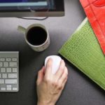 Close up of office desk with keyboard, mouse, coffee cup, red purse and green planner