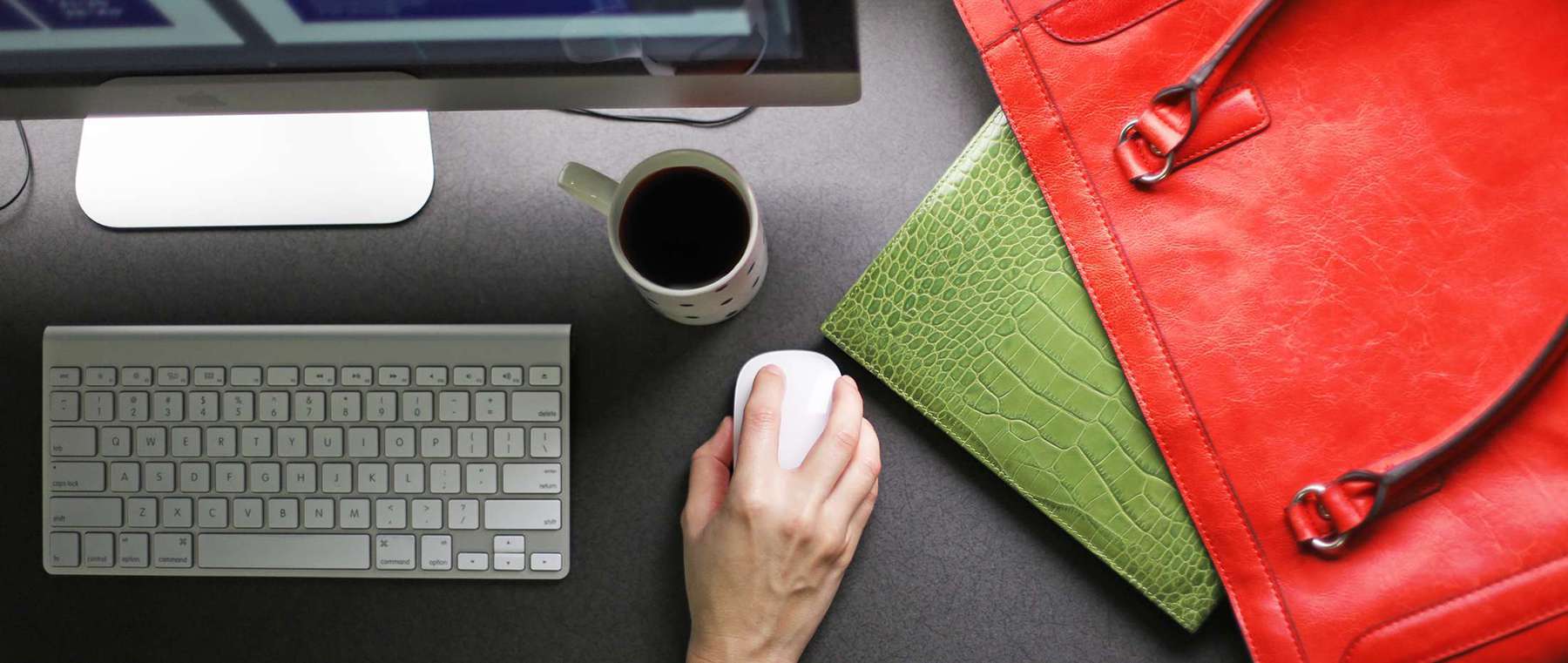 Close up of office desk with keyboard, mouse, coffee cup, red purse and green planner